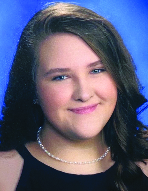 A young woman with long wavy hair, wearing a black dress and a pearl necklace, smiling against a blue background.